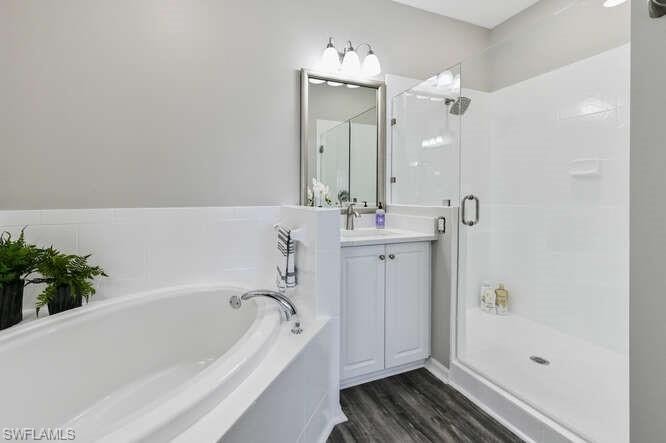 Full bath with a bath, vanity, a shower stall, and dark wood-style floors