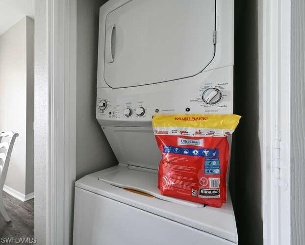 Laundry room with stacked washer and clothes dryer and dark wood-style flooring