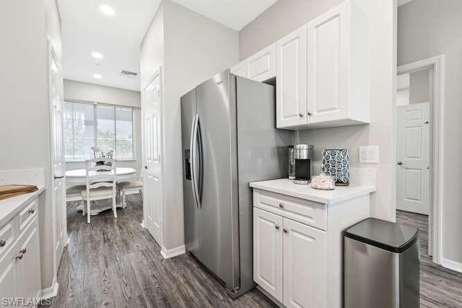 Kitchen with light countertops, white cabinets, dark wood-type flooring, stainless steel fridge, and recessed lighting