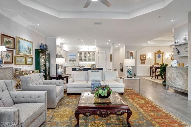 Living room featuring a raised ceiling, ornamental molding, recessed lighting, wood finished floors, and a ceiling fan