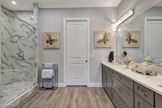 Featuring a frameless glass enclosed frameless shower, porcelain tiled flooring, vanity with dual sinks, and quartz countertopsvanity, porcelain tile plank wood like floor,  crown molding and walk-in-closet