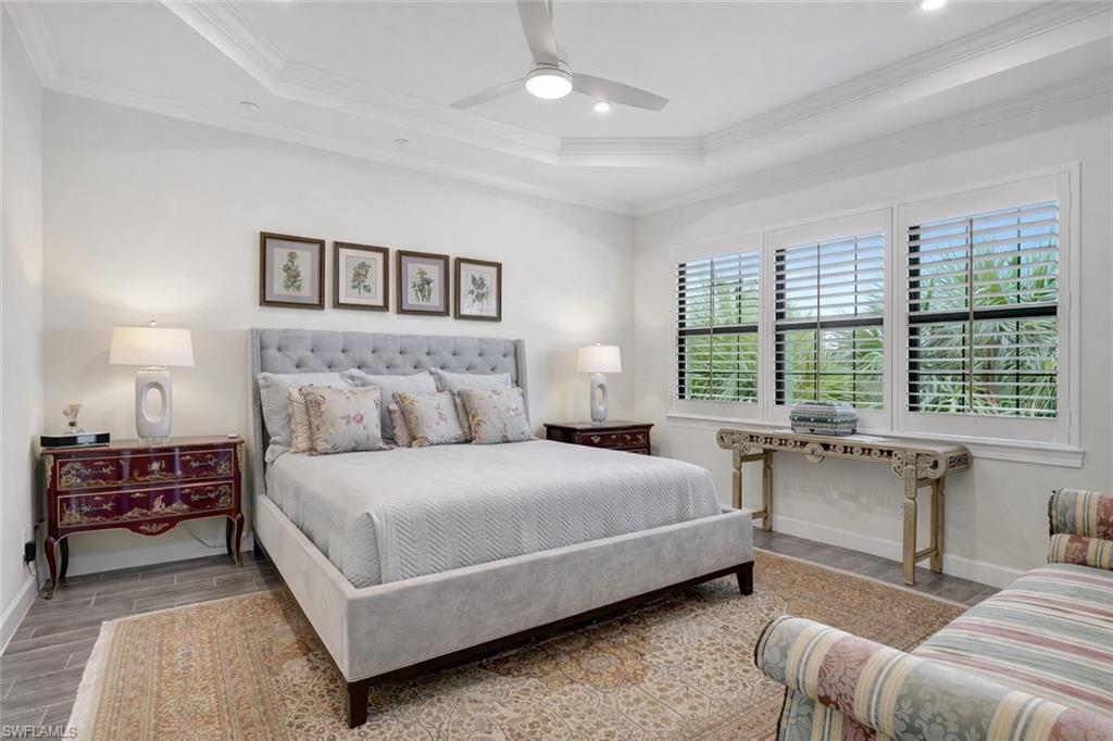 Primary Bedroom with porcelain wood-like flooring, ceiling fan, crown molding, tray ceiling, with recessed lighting and sweeping serene views of the lake and preserves