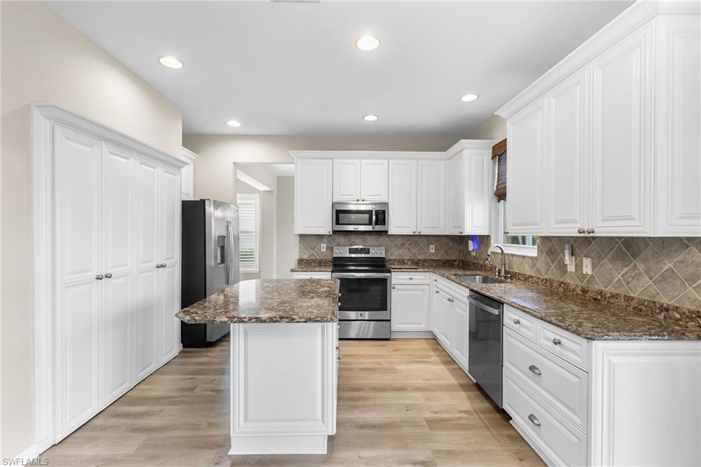 Kitchen with white cabinets, appliances with stainless steel finishes, dark stone countertops, light wood finished floors, and backsplash