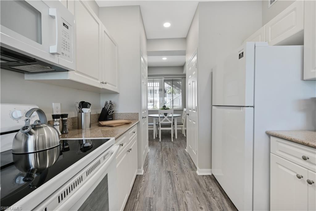 Kitchen featuring white appliances, white cabinets, light wood finished floors, light stone counters, and recessed lighting