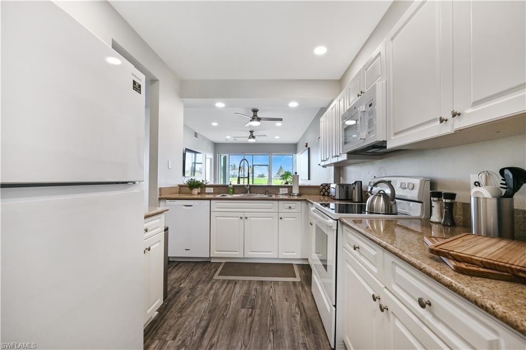 Kitchen with white appliances, white cabinetry, light stone countertops, recessed lighting, and dark wood finished floors