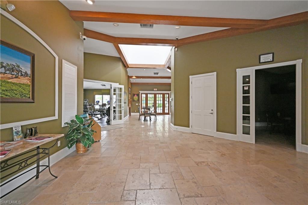 Hallway with french doors, stone tile floors, beam ceiling, recessed lighting, and a high ceiling