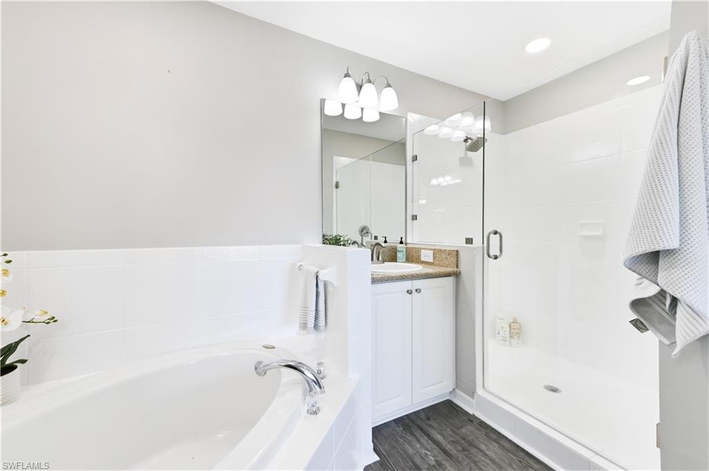 Full bathroom with vanity, a bath, a stall shower, and dark wood-type flooring