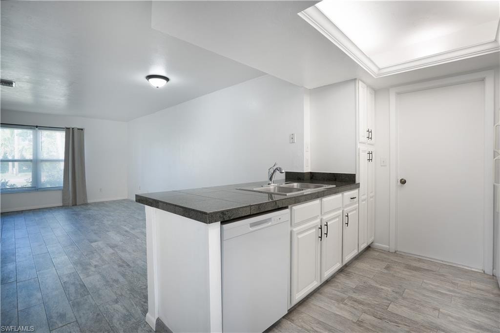 Kitchen featuring a peninsula, dishwasher, light wood-style flooring, and white cabinets