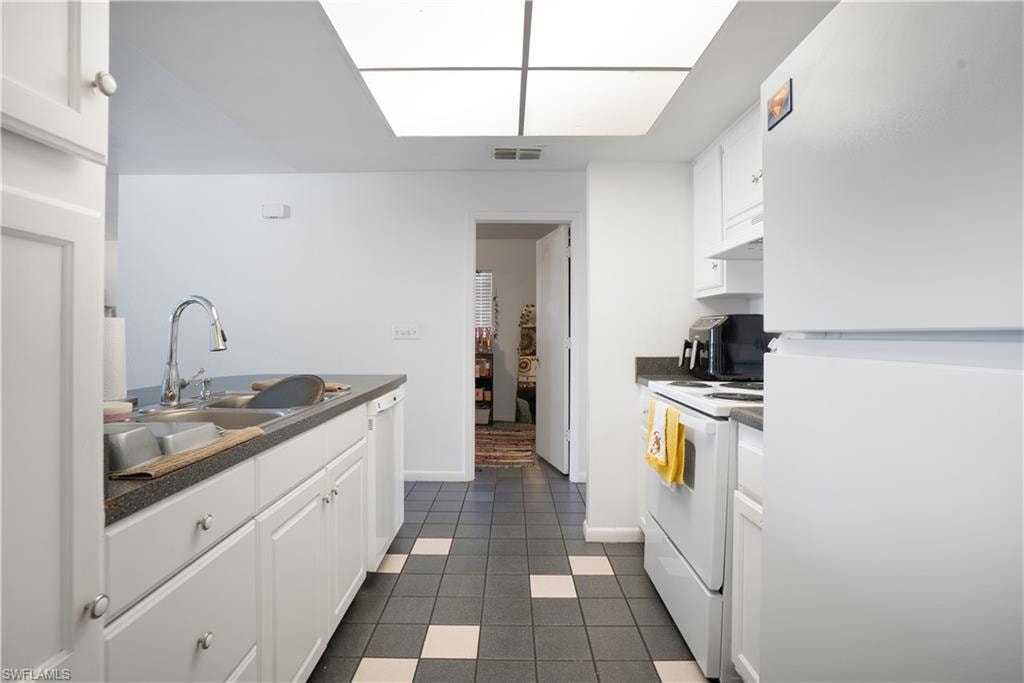 Kitchen with dark countertops, white appliances, white cabinets, and dark tile patterned flooring