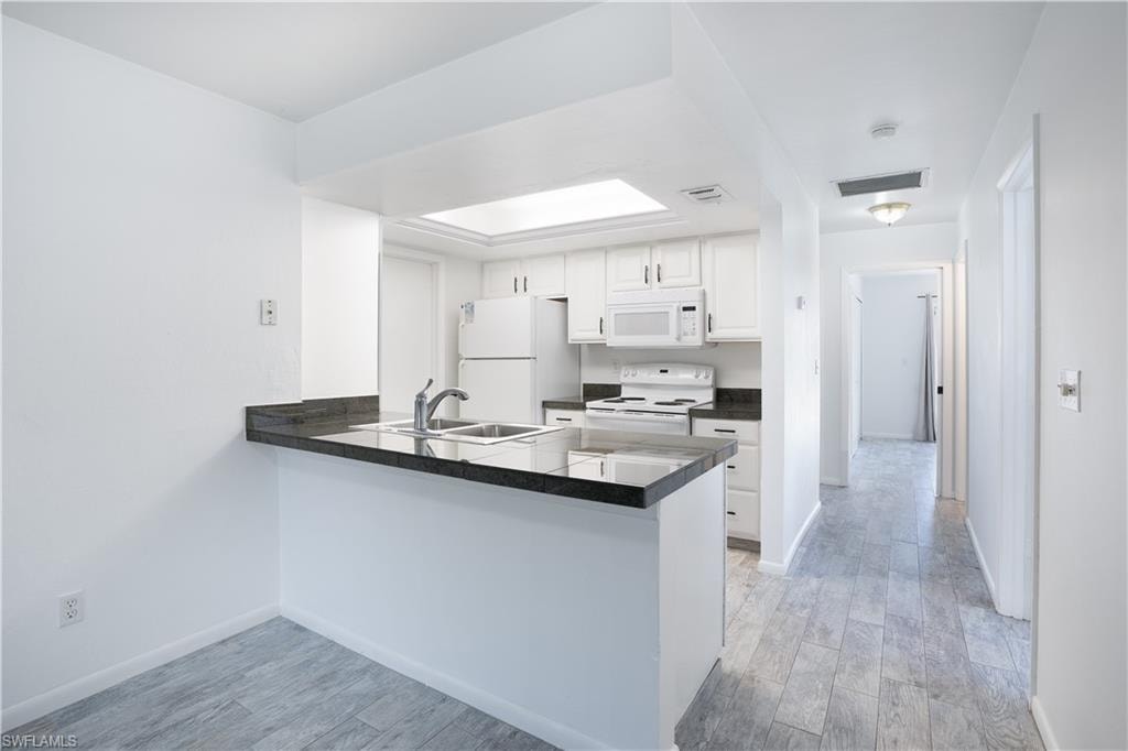 Kitchen featuring white cabinets, white appliances, a peninsula, and light wood-style floors