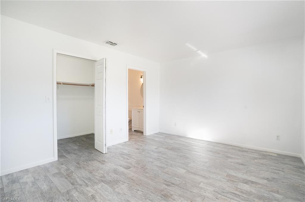 Unfurnished bedroom featuring a spacious closet, connected bathroom, and light wood-style floors