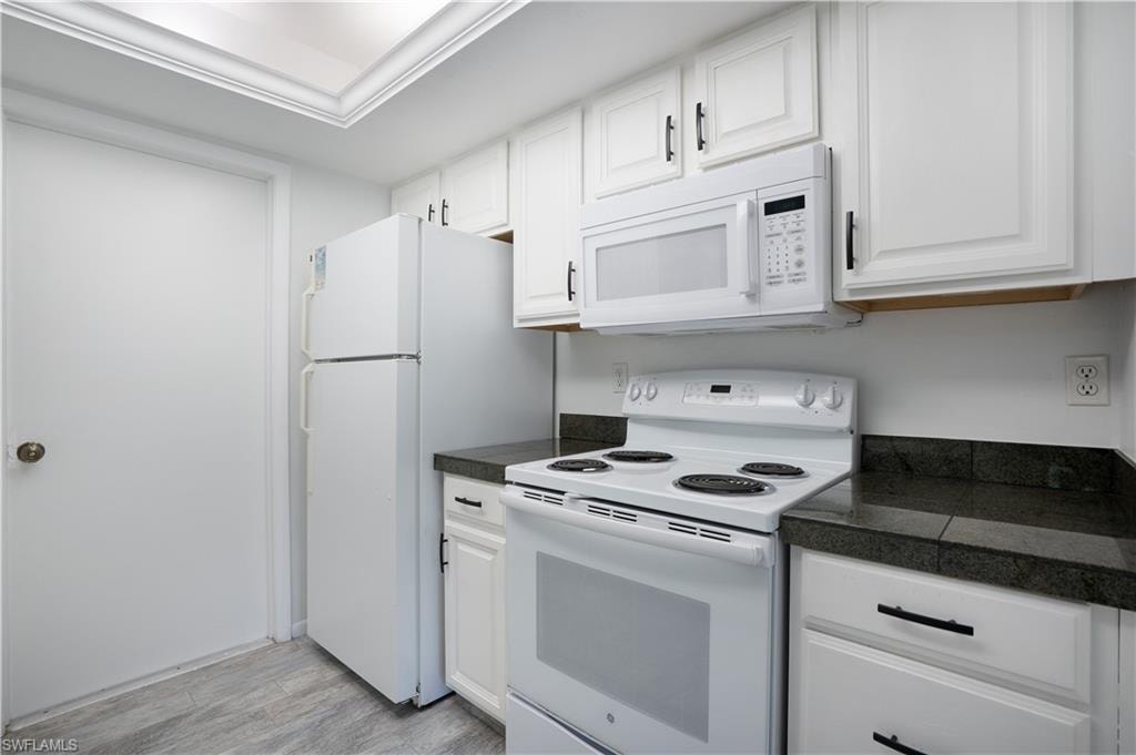 Kitchen featuring white appliances, white cabinets, light wood-style flooring, and tile countertops