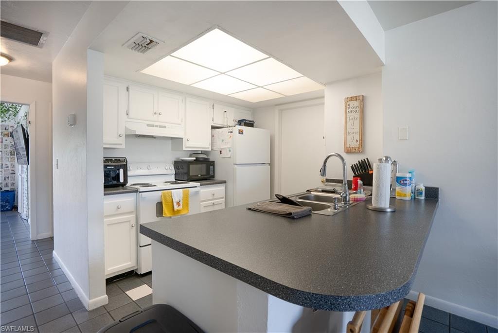 Kitchen featuring dark countertops, white appliances, a peninsula, white cabinetry, and a breakfast bar area