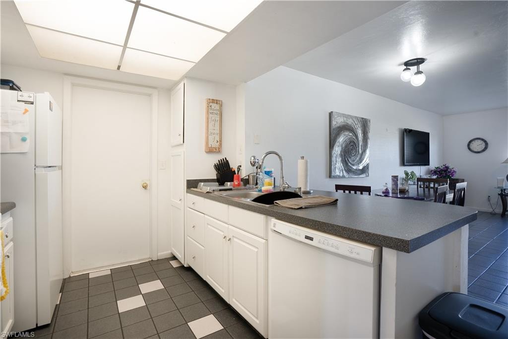 Kitchen featuring a peninsula, white appliances, dark tile patterned floors, dark countertops, and white cabinetry