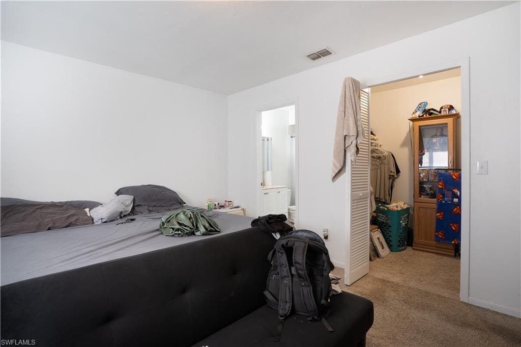 Bedroom with light colored carpet, a walk in closet, and connected bathroom