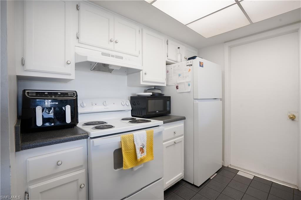 Kitchen with white appliances, dark countertops, white cabinetry, and dark tile patterned flooring