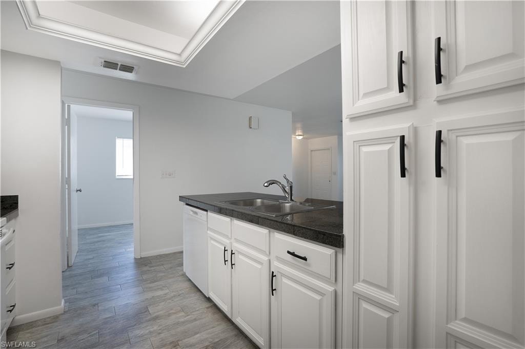 Kitchen featuring white cabinetry, light wood-type flooring, white dishwasher, a peninsula, and tile counters