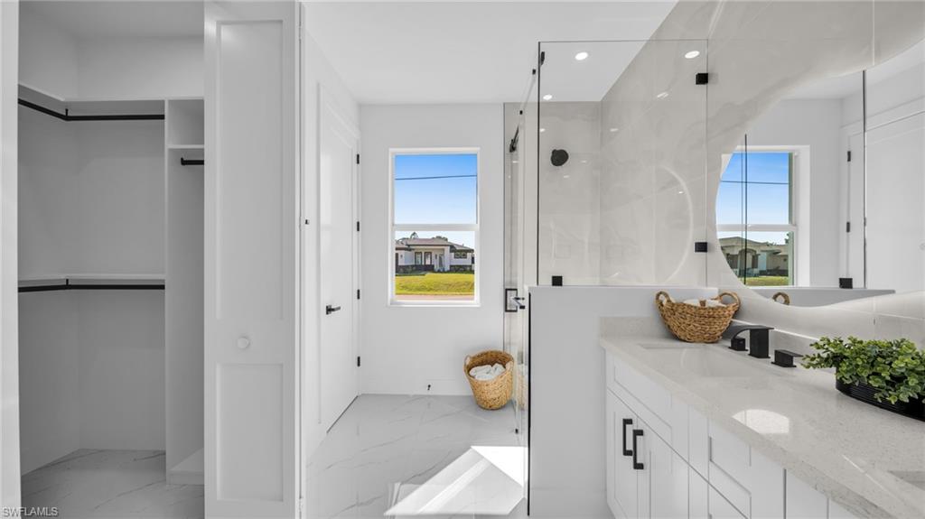 Full bathroom featuring a spacious closet, a marble finish shower, double vanity, light marble finish flooring, and recessed lighting