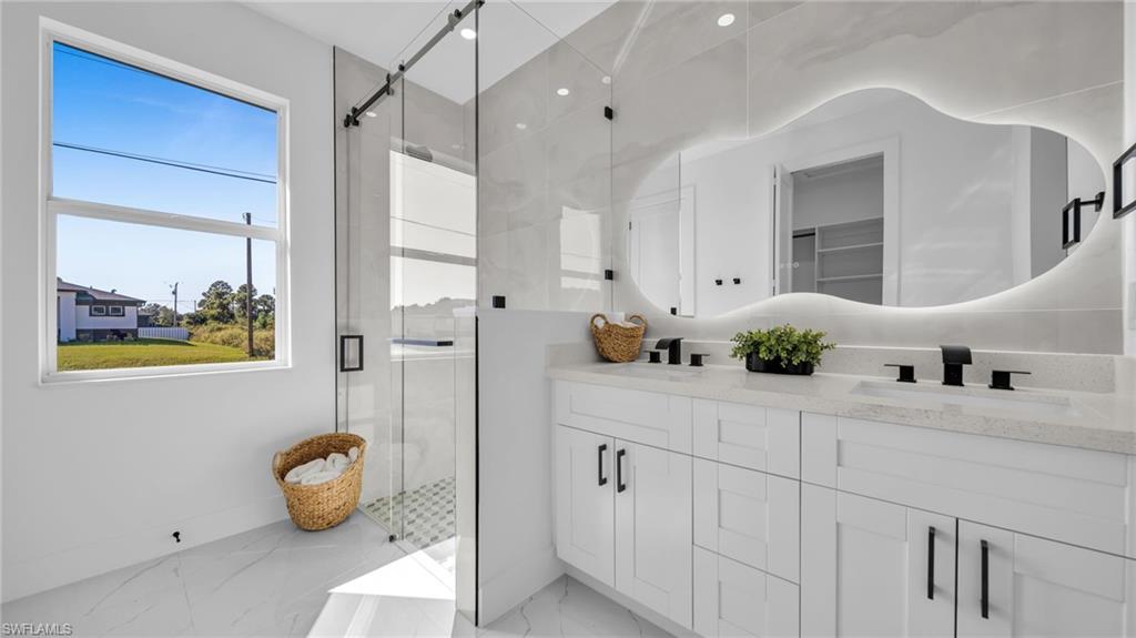 Bathroom featuring a shower stall, double vanity, and light marble finish floors