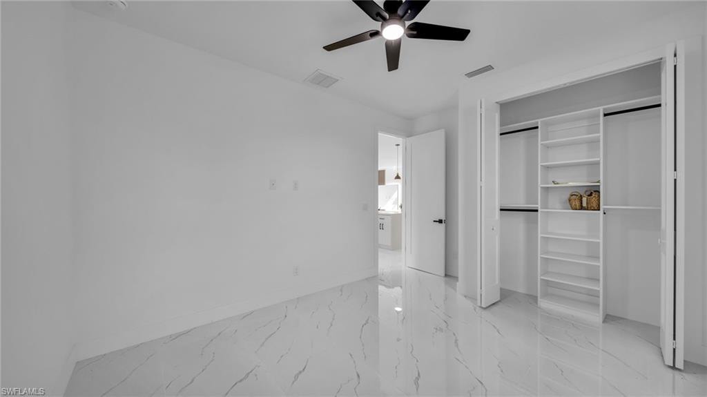Unfurnished bedroom featuring light marble finish flooring, ceiling fan, and a closet