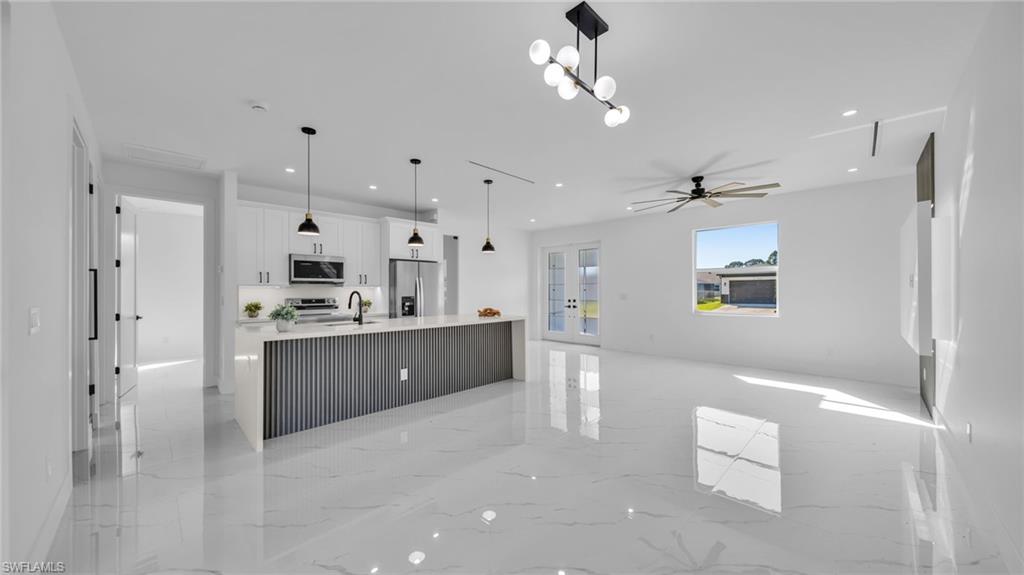 Kitchen with white cabinetry, open floor plan, light marble finish floors, a large island with sink, and hanging light fixtures