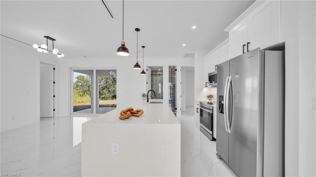Kitchen featuring appliances with stainless steel finishes, light marble finish flooring, pendant lighting, recessed lighting, and an island with sink