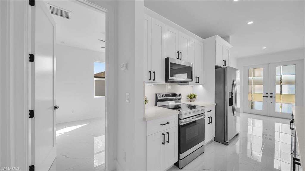 Kitchen with appliances with stainless steel finishes, light marble finish floors, white cabinetry, plenty of natural light, and recessed lighting