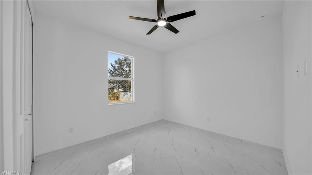 Unfurnished bedroom featuring marble look tiles, a ceiling fan, and a closet