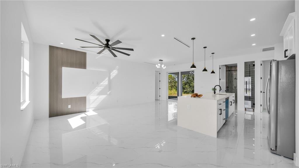 Kitchen featuring light marble finish floors, a kitchen island with sink, open floor plan, pendant lighting, and freestanding refrigerator