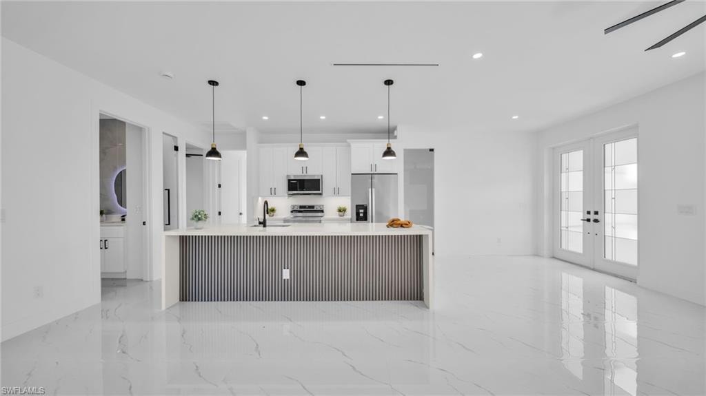 Kitchen with white cabinetry, appliances with stainless steel finishes, french doors, light stone counters, and a large island