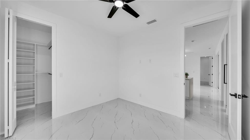 Unfurnished bedroom with a walk in closet, light marble finish flooring, and ceiling fan