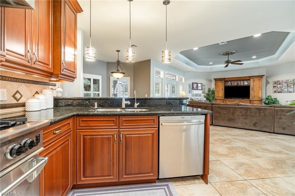 Kitchen with a raised ceiling, dark stone counters, a peninsula, stainless steel appliances, and pendant lighting