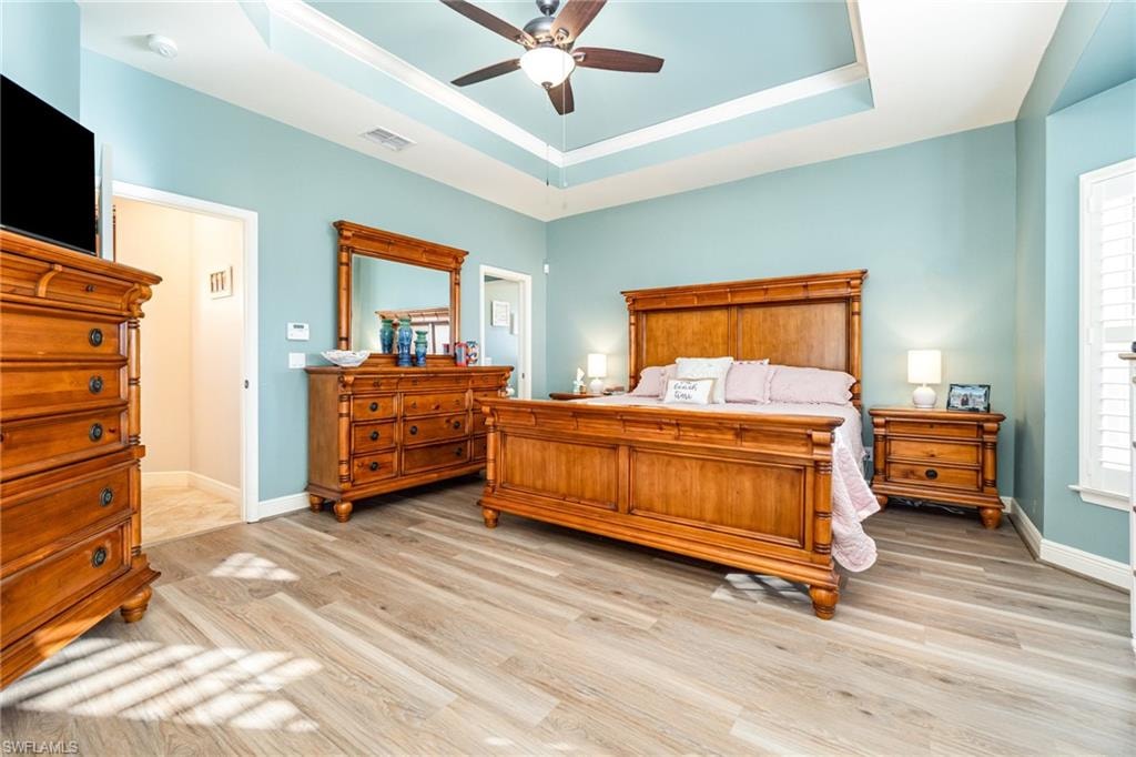 Bedroom featuring a tray ceiling, light wood finished floors, and a ceiling fan
