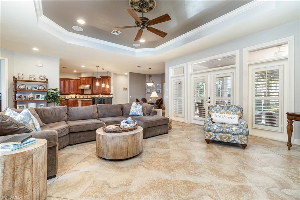 Living room with a raised ceiling, recessed lighting, ornamental molding, ceiling fan, and light tile patterned floors