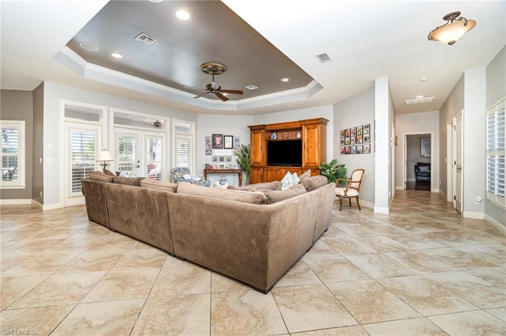 Living area with a raised ceiling, ceiling fan, recessed lighting, and light tile patterned flooring