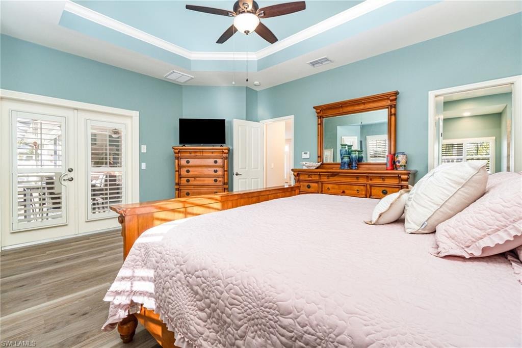 Bedroom featuring a raised ceiling, wood finished floors, ceiling fan, crown molding, and access to exterior