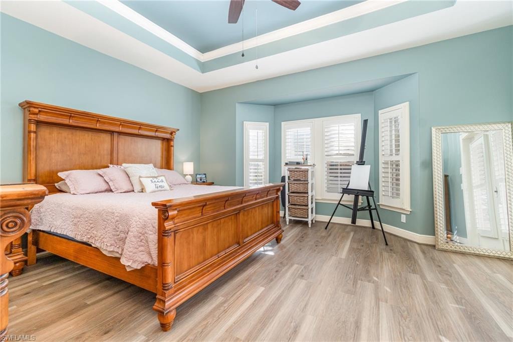 Bedroom with a tray ceiling, light wood-style flooring, and a ceiling fan