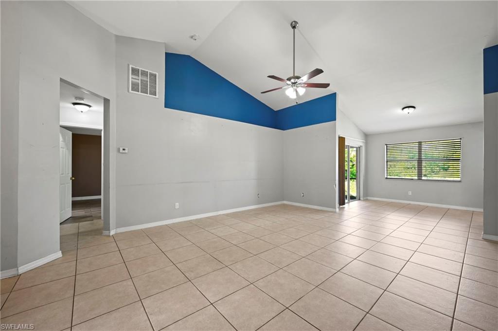 Empty room with high vaulted ceiling, light tile patterned flooring, and ceiling fan