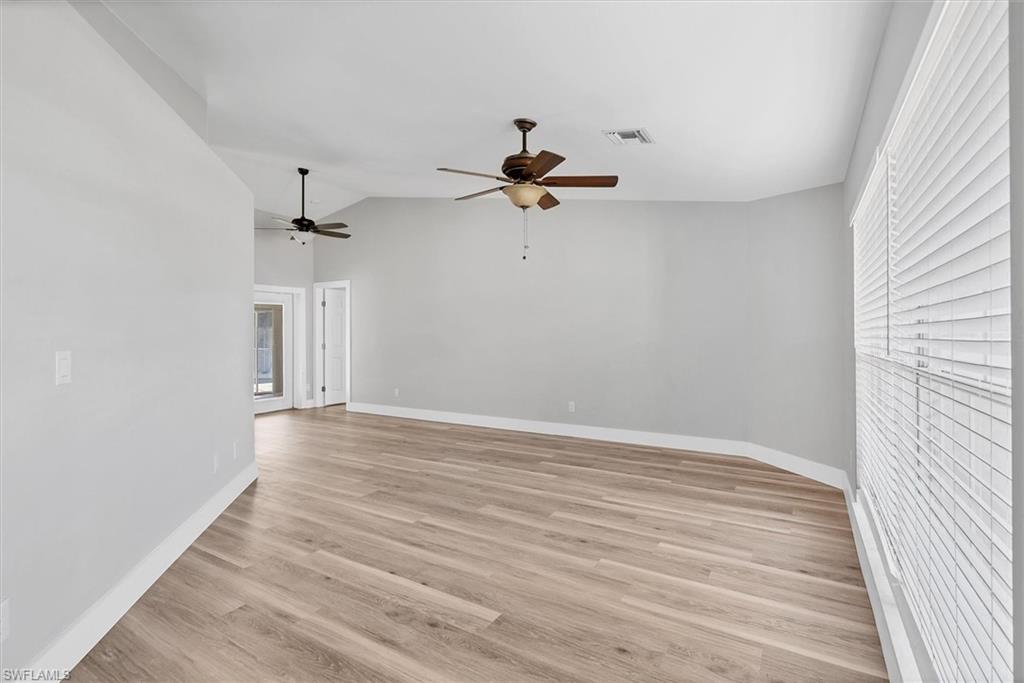 Empty room with light wood-style floors, vaulted ceiling, plenty of natural light, and a ceiling fan
