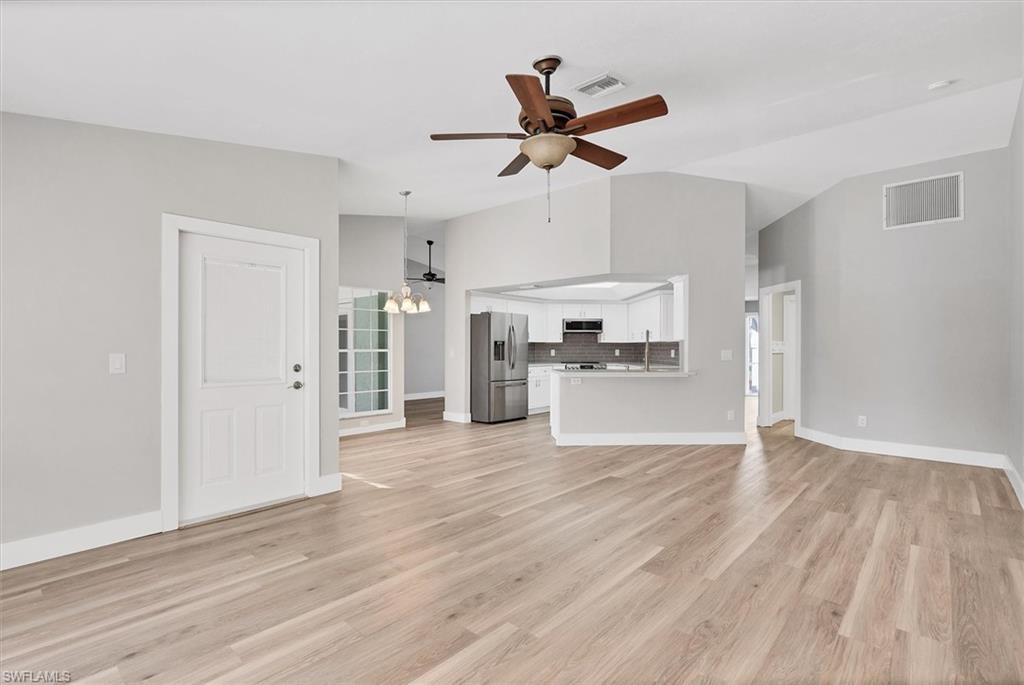 Unfurnished living room featuring vaulted ceiling, a chandelier, ceiling fan, and light wood-style flooring