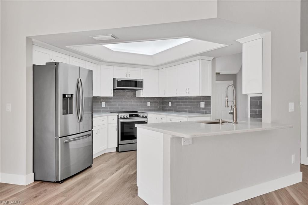 Kitchen featuring appliances with stainless steel finishes, white cabinets, a peninsula, and tasteful backsplash