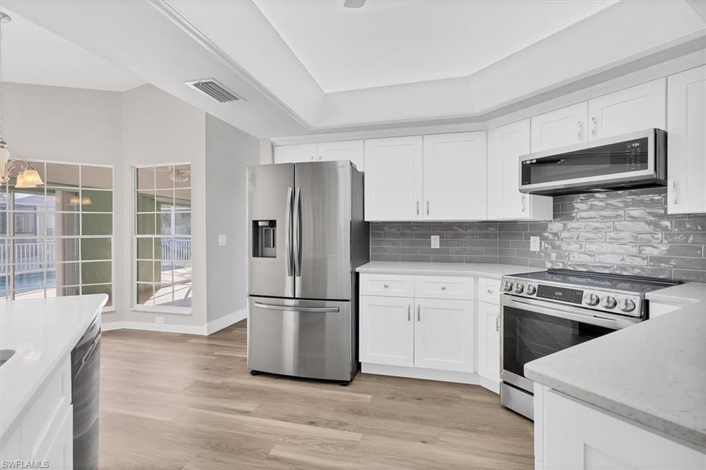 Kitchen featuring appliances with stainless steel finishes, white cabinetry, light stone counters, and light wood-style floors