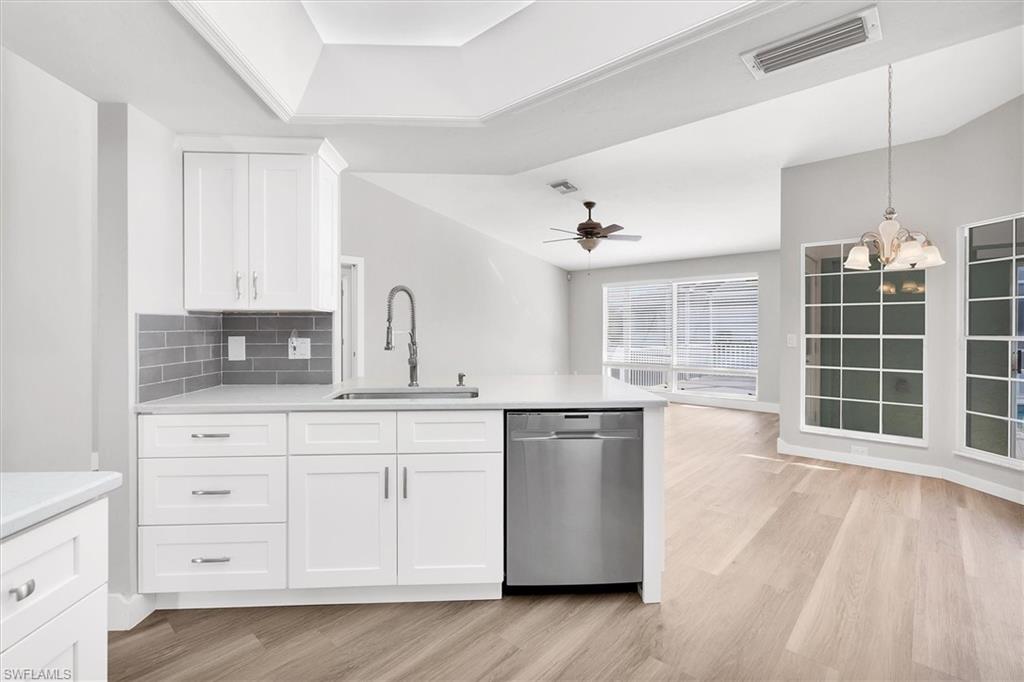 Kitchen with white cabinetry, dishwasher, backsplash, and light wood-style flooring