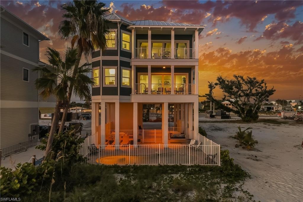 Back of house at dusk with stucco siding, a metal roof, a sunroom, and a balcony
