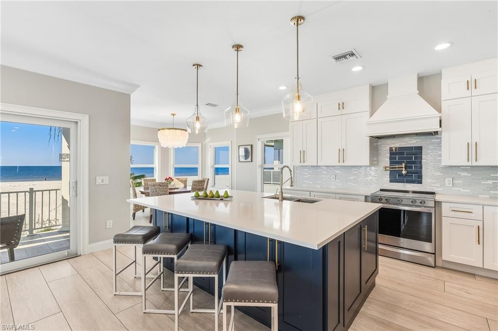 Kitchen with electric stove, white cabinetry, premium range hood, decorative backsplash, and decorative light fixtures