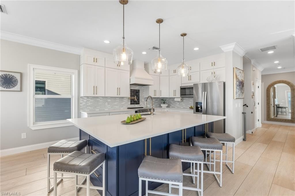 Kitchen with ornamental molding, white cabinets, a kitchen bar, decorative light fixtures, and a center island with sink