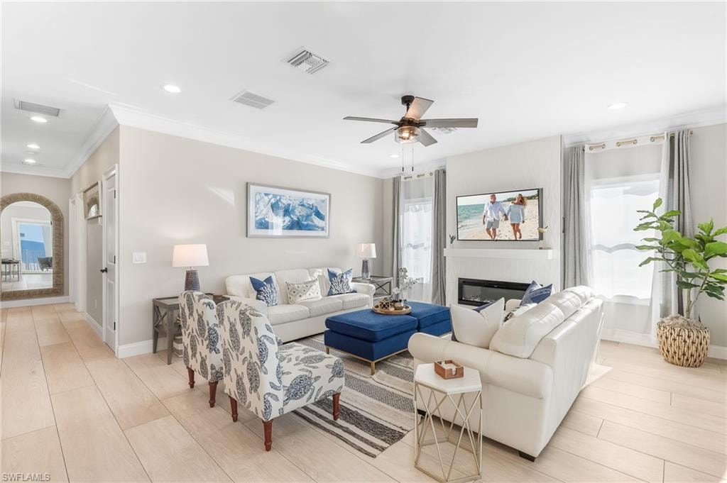 Living room featuring crown molding, light wood-type flooring, ceiling fan, a glass covered fireplace, and recessed lighting