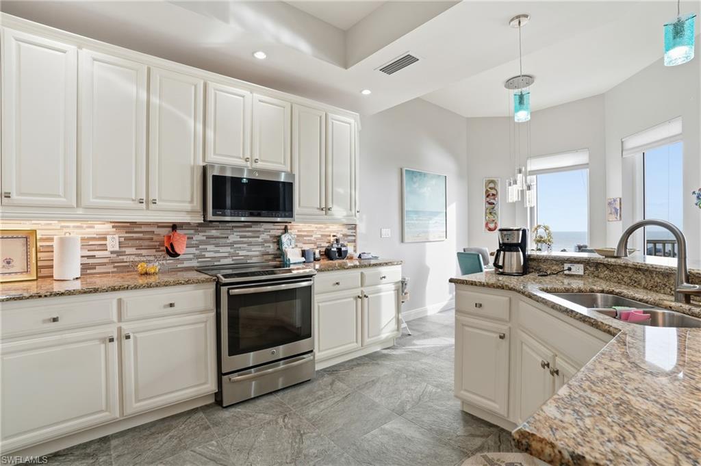 Kitchen with white cabinetry, light stone countertops, stainless steel appliances, hanging light fixtures, and recessed lighting - Virtually Edited Image