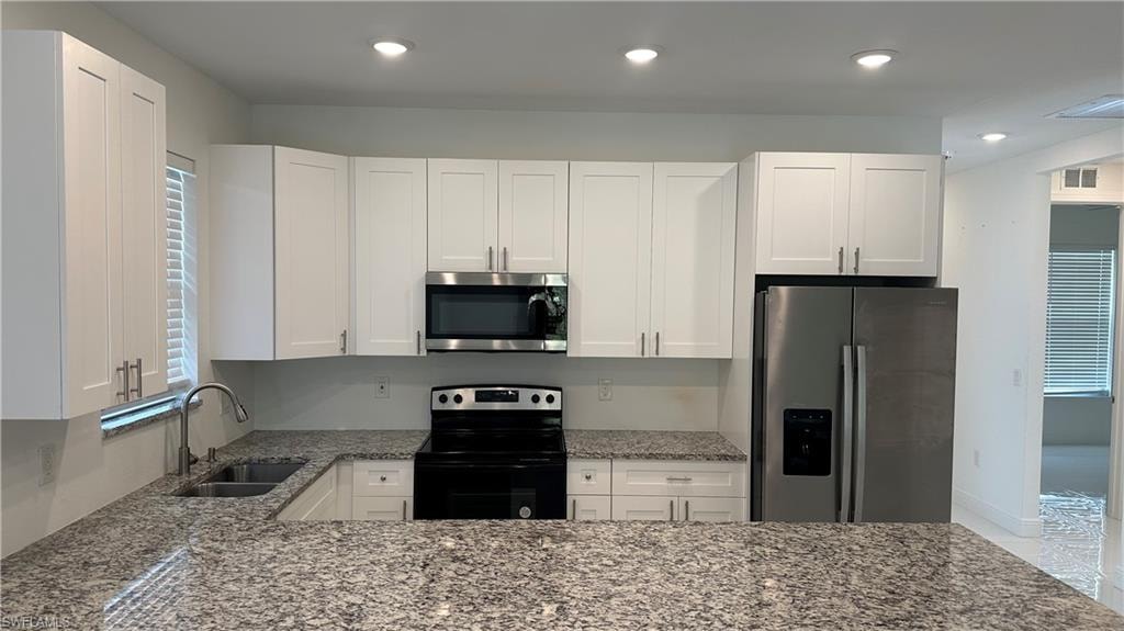 Kitchen with healthy amount of natural light, light stone countertops, stainless steel appliances, white cabinets, and recessed lighting
