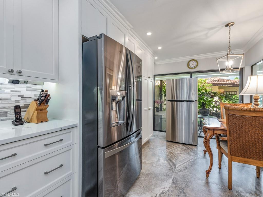 Kitchen with stainless steel refrigerator with ice dispenser, freestanding refrigerator, white cabinets, a barn door, and decorative light fixtures